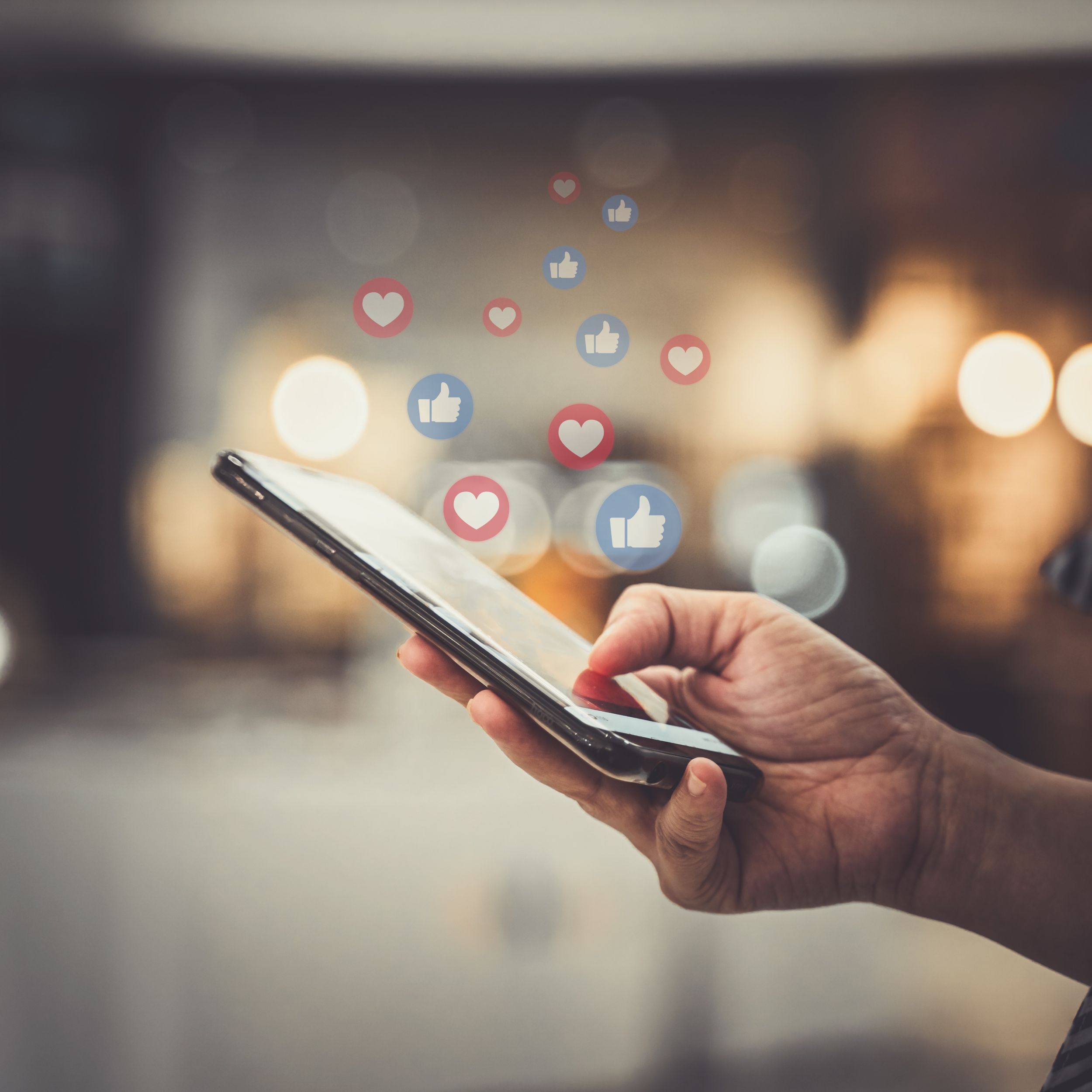 Social Media Optimization - photo shows hand holding a phone, thumb clicking on likes and loves